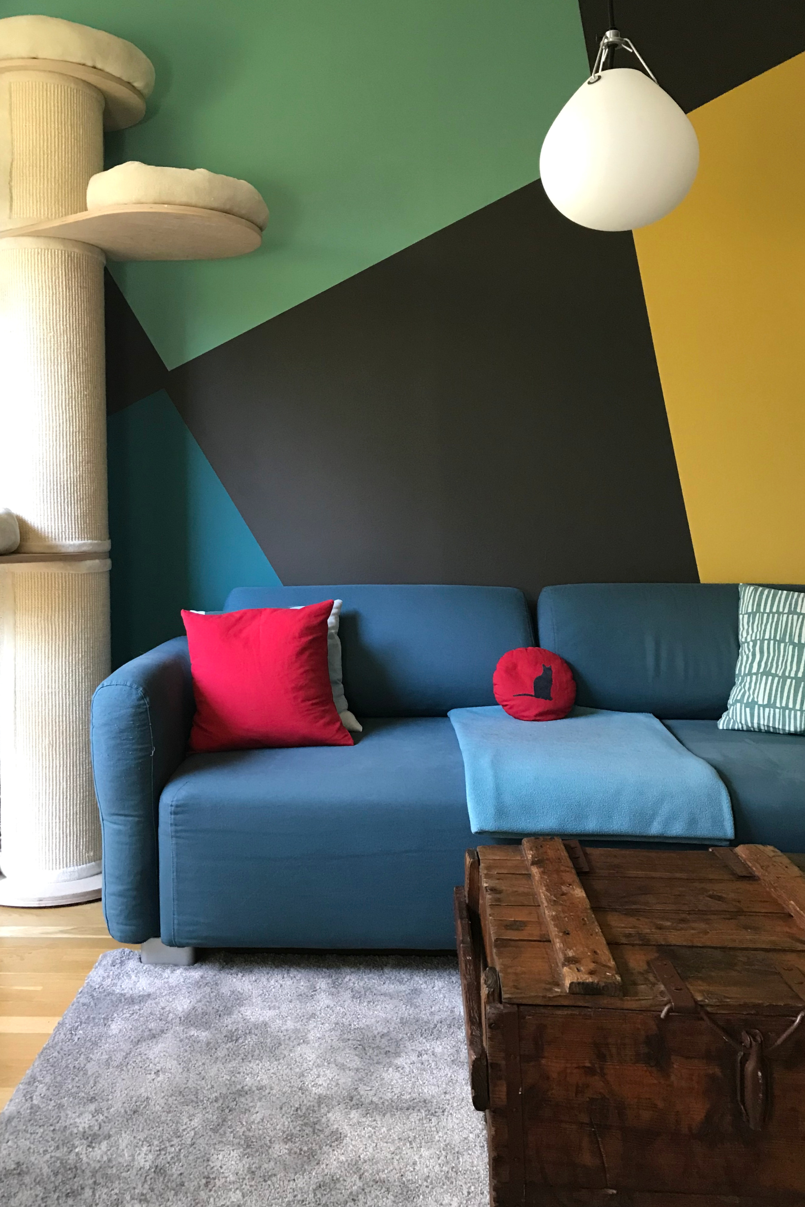 Wandmalerei in Wohnzimmer mit geometrischen Formen vor einem Sofa.