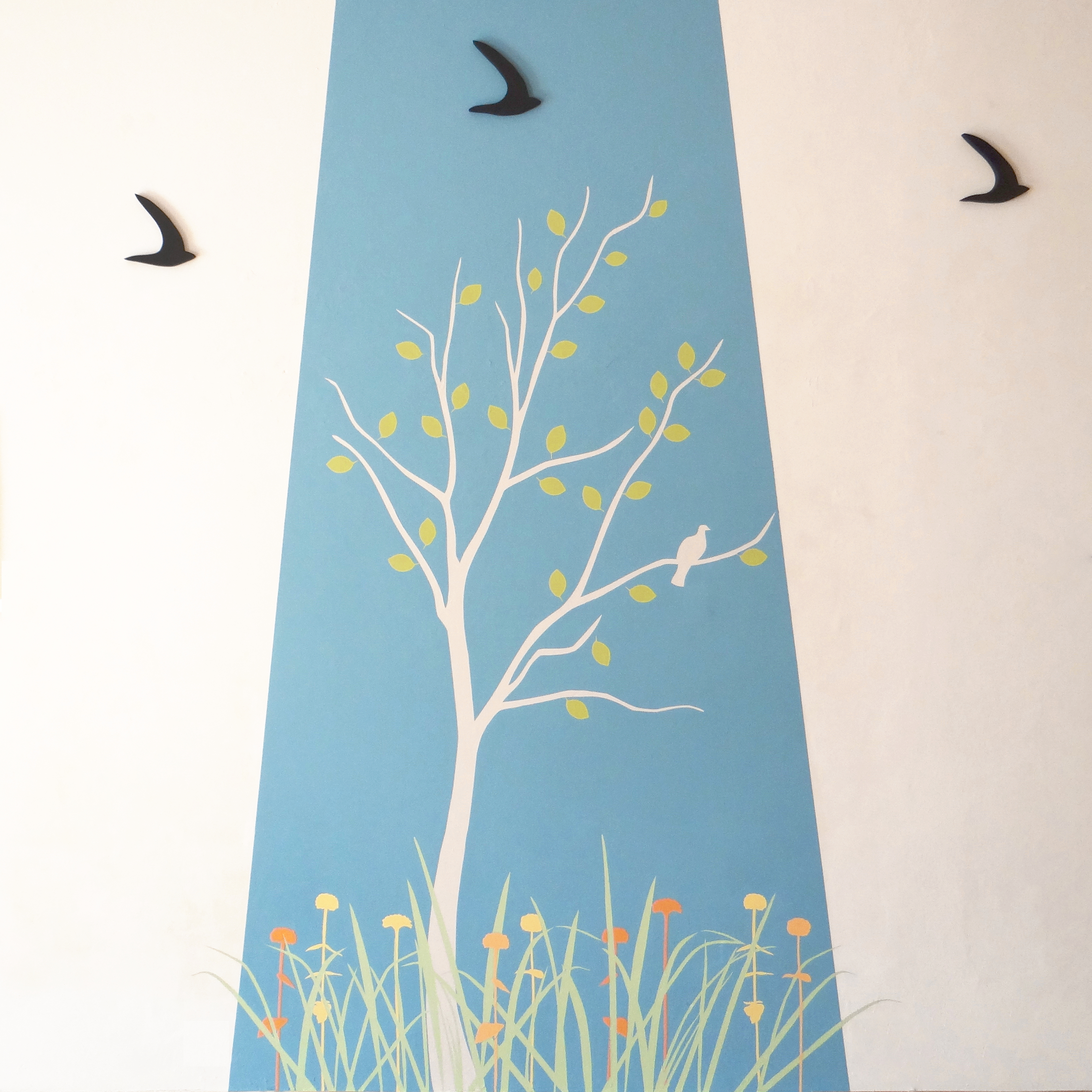 Wandmalerei bestehend aus hellgrauem Baum vor hellblauem Hintergrund. Unter dem Baum ist eine Wiese mit Blumen. 